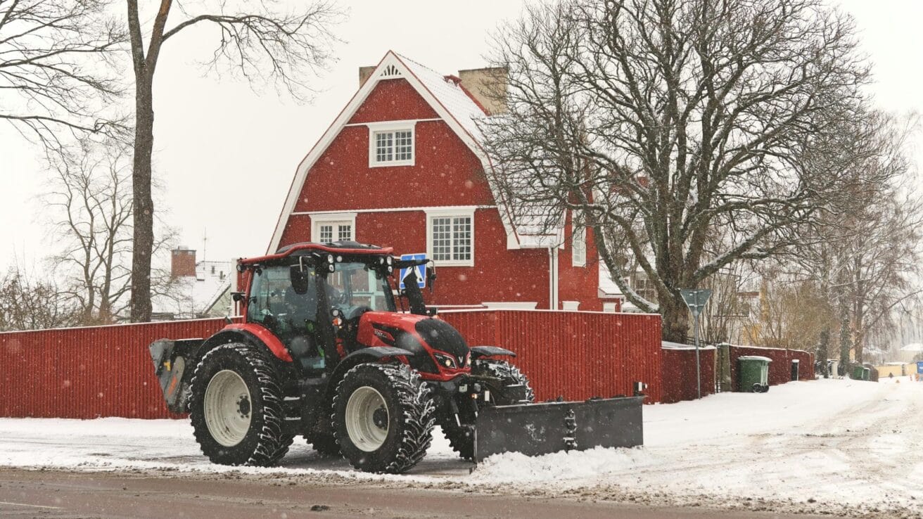 A red tractor plowing snow near a traditional red house in Jönköping, Sweden.